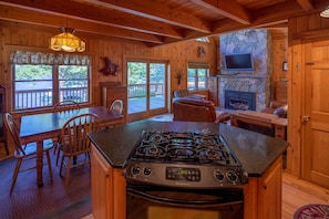 A wooden cabin interior with a kitchen, dining area, and fireplace. - Large Lakefront Home (Rangeley)