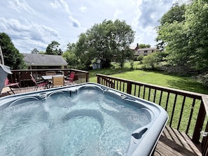 A hot tub on a wooden deck with a grassy yard and a house in the background.
