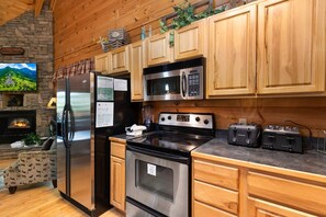 A modern kitchen with wooden cabinets, a stainless steel refrigerator, a microwave, a stove, and two toasters.