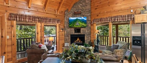 A log cabin interior with a fireplace, wooden furniture, and a stone fireplace surround.
