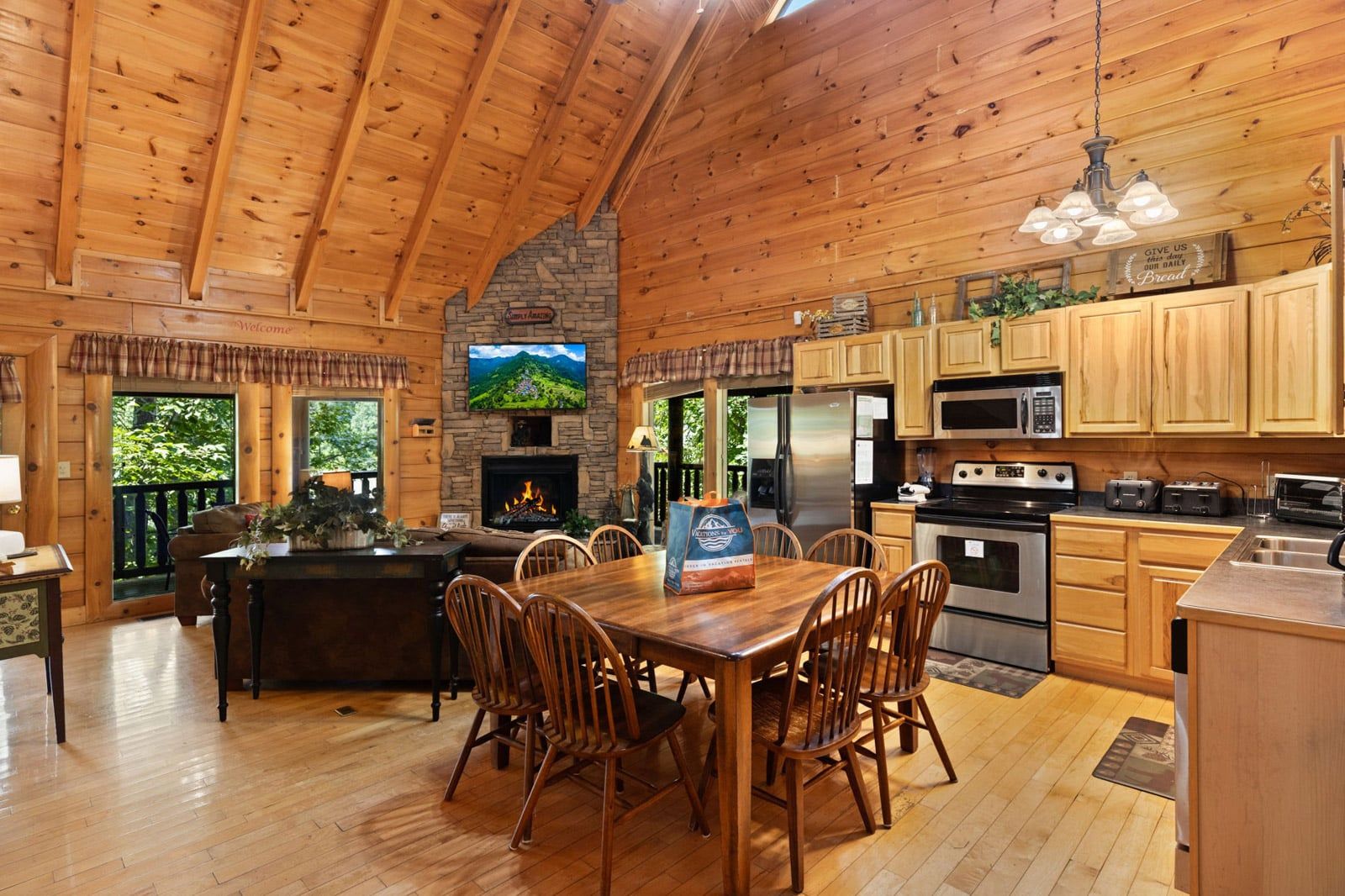 A wooden cabin interior with a dining area, kitchen, fireplace, and a TV mounted on the wall.