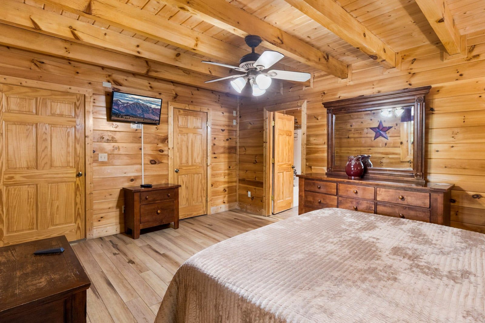 A wooden cabin room with a bed, dresser, and a ceiling fan.