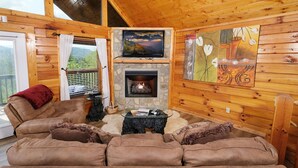 A cozy cabin interior with a stone fireplace, a television mounted above it, and a large window with curtains. - Edge of Paradise - Private Indoor Pool, Hot Tub (Pigeon Forge)