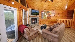 A cozy cabin interior with a fireplace, leather couches, a television, and a balcony with a view of the outdoors. - Edge of Paradise - Private Indoor Pool, Hot Tub (Pigeon Forge)