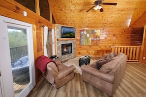 Ein gemütliches Blockhaus-Interieur mit Kamin, Ledersofas, einem Fernseher und einem Balkon mit Blick ins Freie.