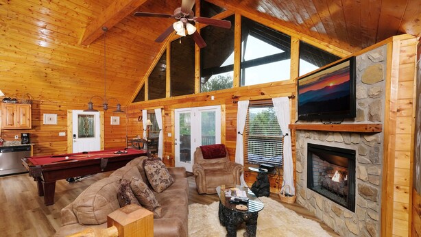 A cozy cabin interior with a pool table, leather sofa, stone fireplace, and a television mounted on the wall. - Edge of Paradise - Private Indoor Pool, Hot Tub (Pigeon Forge)