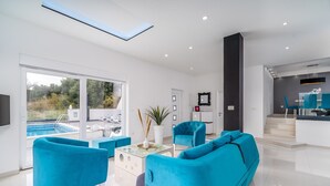 Een moderne woonkamer met uitzicht op een zwembad, heldere verlichting en een trap naar een eetgedeelte.