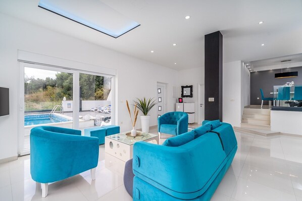 Una sala de estar moderna con vista a la piscina, iluminación brillante y una escalera que lleva a un comedor.