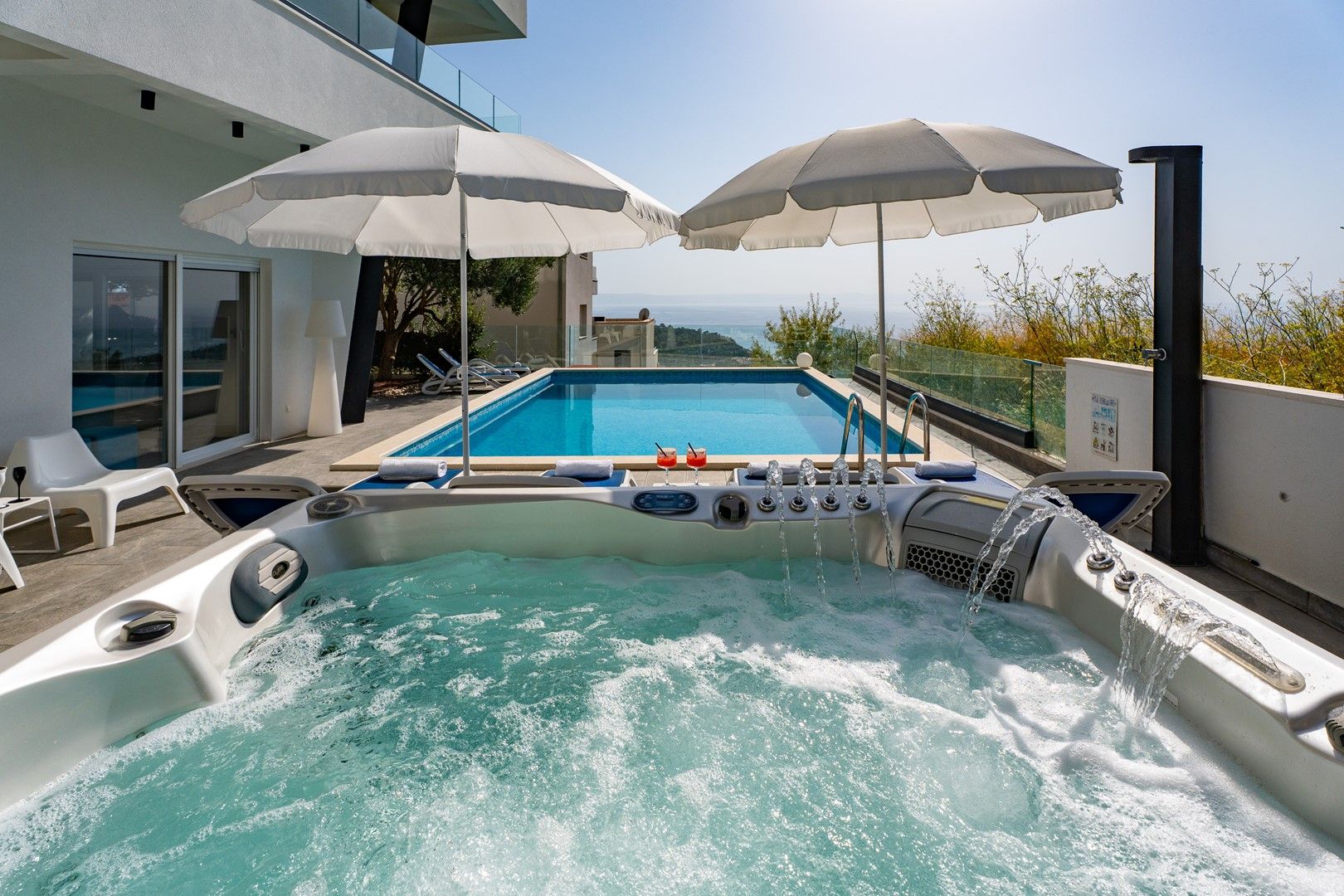 Un jacuzzi con vista a una piscina y al mar, rodeado de sombrillas y sillas de descanso.