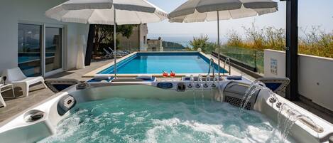 Un jacuzzi con vista a una piscina y al mar, rodeado de sombrillas y sillas de descanso.