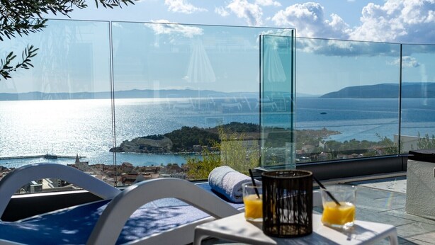 Een balkon met een glazen balustrade, een tafel met twee glazen sinaasappelsap en een stoel met een handdoek.