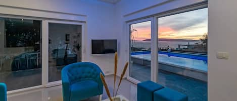 A modern living room with a large window overlooking a pool and a sunset view.