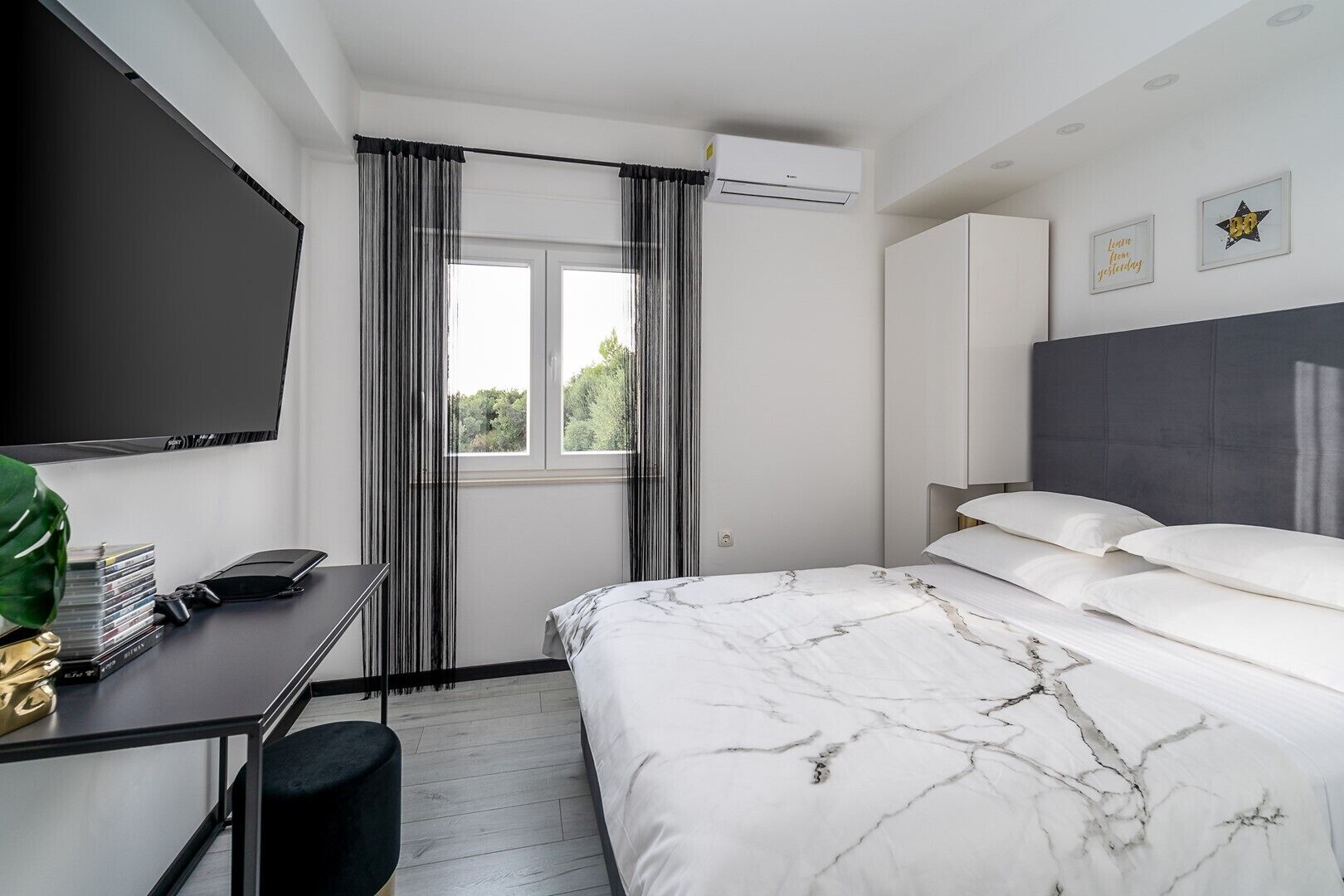 Une chambre moderne avec un lit, un bureau, une télévision et une fenêtre avec des rideaux.