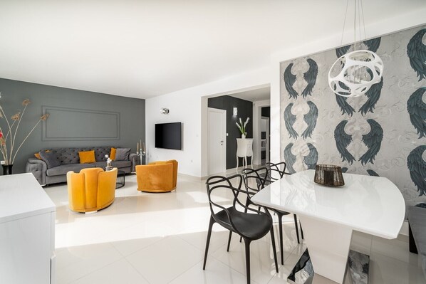 Un soggiorno moderno con un divano grigio, un pouf giallo e un tavolo da pranzo bianco con sedie nere.
