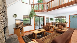 A spacious living room with a stone wall, wooden furniture, and large windows offering a view of the outdoors.