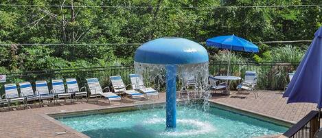 Un área de piscina con fuente de agua, sillas de descanso y una sombrilla azul.