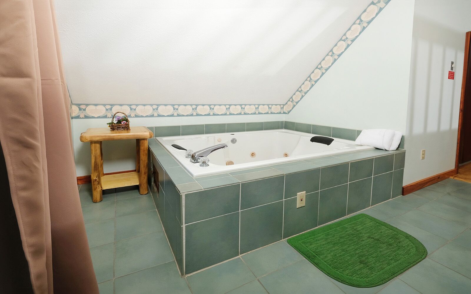 A bathroom with a large bathtub, a wooden stool, and a green rug.