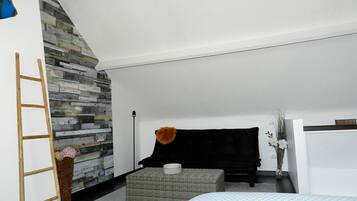 Un dormitorio moderno con una pared de acento de piedra, una cama con cubrecama estampado, un pequeño banquito, una silla negra y una escalera apoyada en la pared.