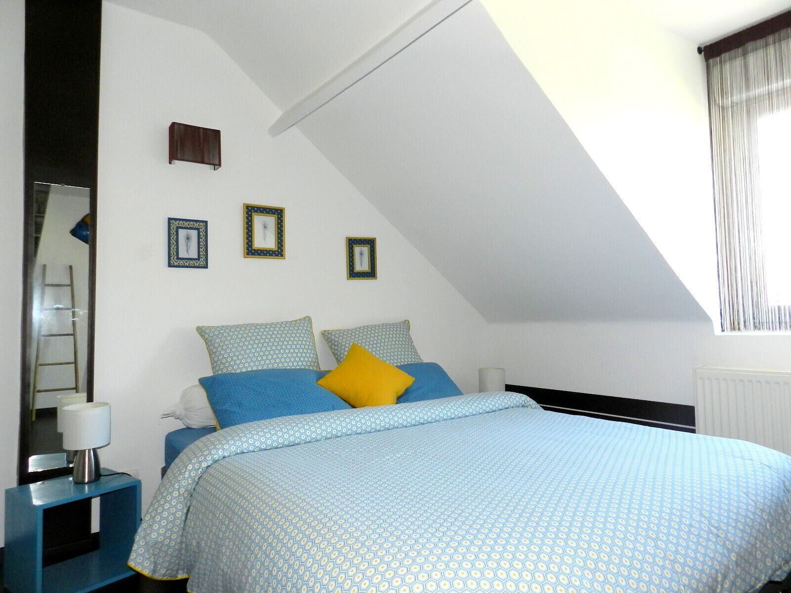Une chambre à coucher avec un lit, une table de chevet, un miroir et une fenêtre avec des rideaux.