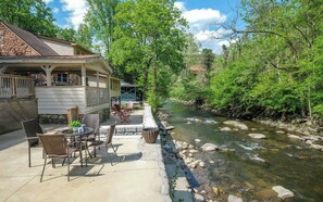 Relax on the patio surrounded by a serene stream and lush greenery.