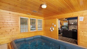 Une cabane en bois dotée d’un bain à remous, de murs en bois et d’une cheminée en pierre.