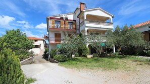 Una casa de dos pisos con balcón, jardín y entrada pavimentada.