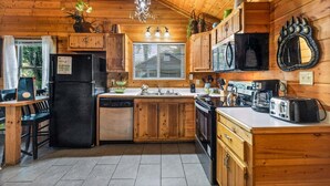 A wooden cabin kitchen with a refrigerator, stove, sink, and a chandelier.