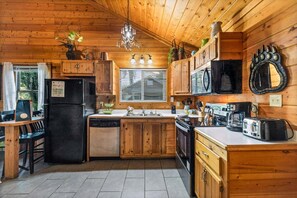 Eine Holzhütte mit Küche, inklusive Kühlschrank, Herd, Spüle und einer Pendelleuchte.