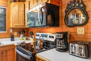 Cocina compacta con armarios de madera, estufa, hervidor, cafetera y tostadora.