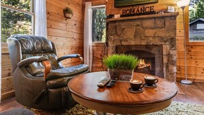 A cozy room with a stone fireplace, leather armchair, and a round wooden table with a plant and two cups of coffee.