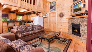 Ein gemütliches Blockhaus-Interieur mit Holzvertäfelung, einem Steinkamin, einer Couch und einem Fernseher, der über dem Kamin angebracht ist.