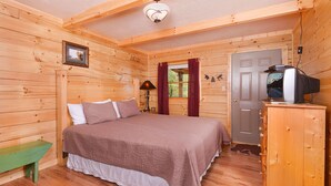 Ein Schlafzimmer einer Holzhütte mit einem Bett, einer Bank, einem Schminktisch und einem Fernseher.