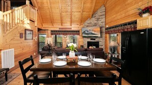 A wooden cabin interior with a dining area, a fireplace, and a living room with a sofa and a TV. - Oh Yea - Pet Friendly, Hot Tub & Games (Sevierville)