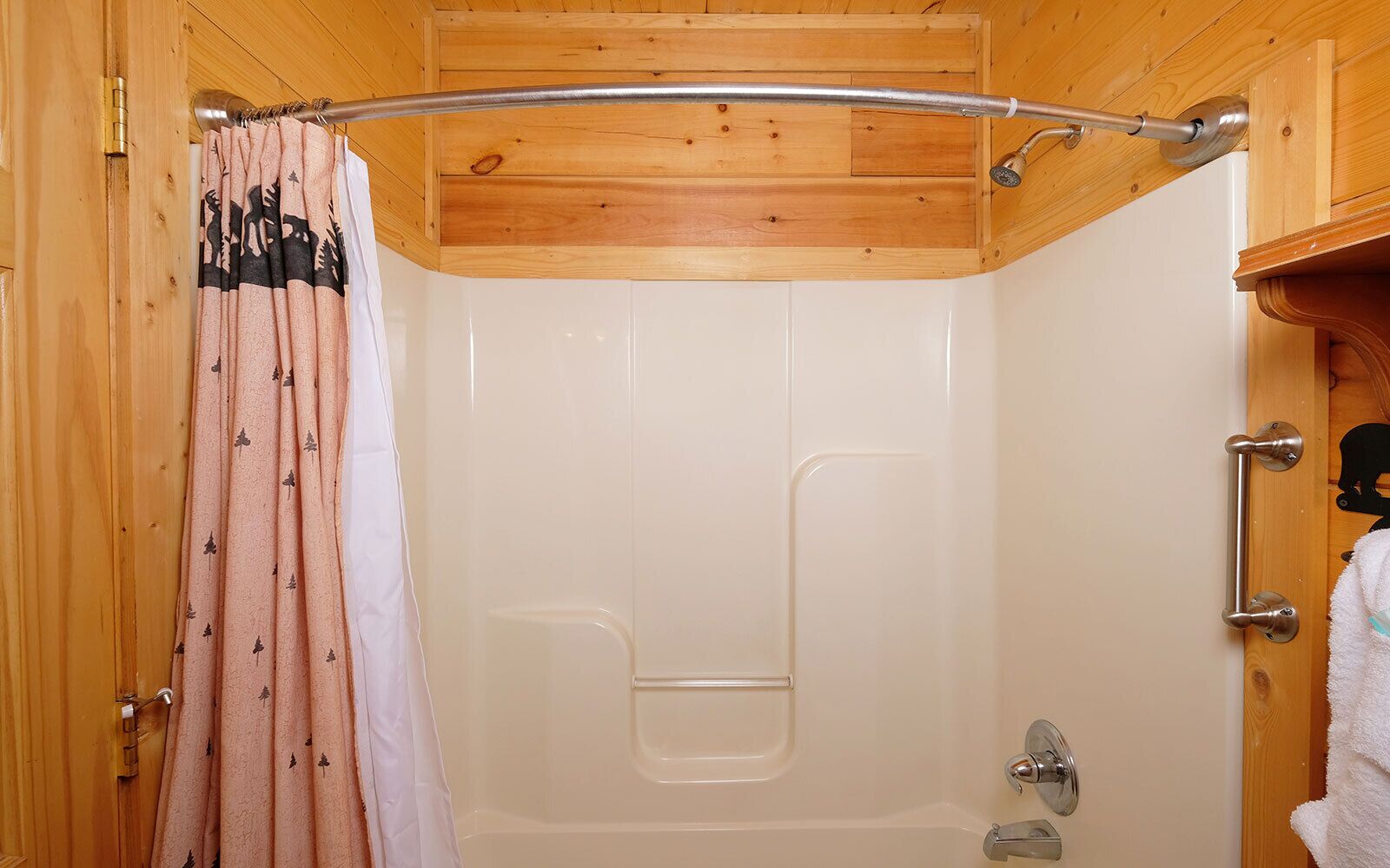 A wooden bathroom with a shower, a towel rack, and a door with a towel hanging on it.