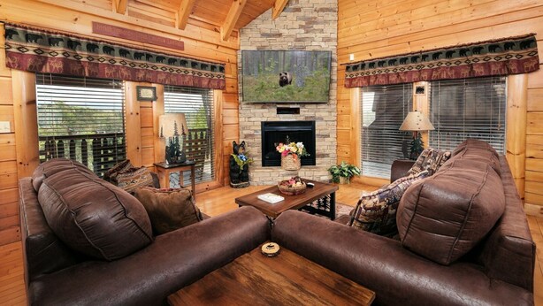 A cozy log cabin interior with a stone fireplace, leather sofas, and a large bear statue. - Oh Yea - Pet Friendly, Hot Tub & Games (Sevierville)