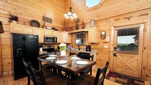 A cozy wooden cabin kitchen with a dining table set for four, a refrigerator, microwave, and a coffee maker. - Oh Yea - Pet Friendly, Hot Tub & Games (Sevierville)