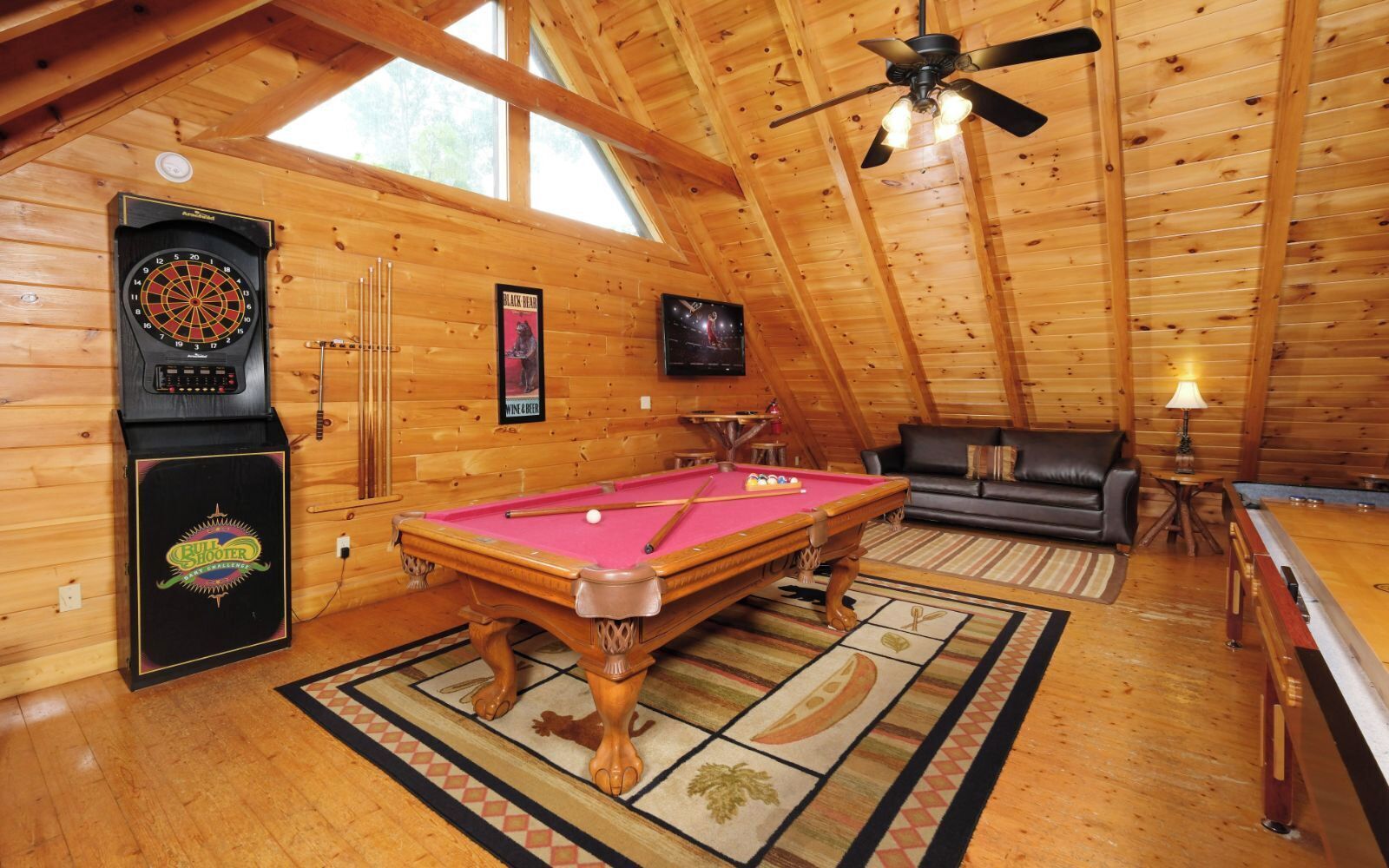 A cozy room with a pool table, a dartboard, a billiards table, and a sofa.