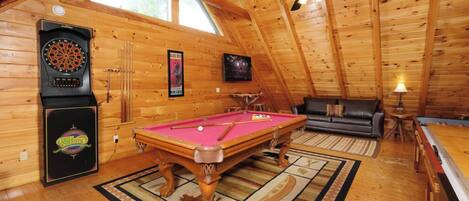 A cozy room with a pool table, a dartboard, a billiards table, and a sofa.