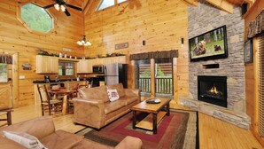 A cozy cabin interior with a living room, kitchen, and fireplace.