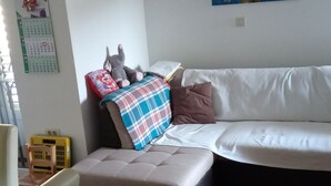 A living room with a white sofa, a small ottoman, a clock, and abstract art on the walls.