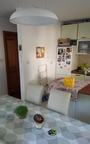 A compact kitchen with a dining table, chairs, a hanging light fixture, a refrigerator, and a small cabinet. - Inviting 2-bed Apartment in Moscenicka Draga (Moscenicka Draga)
