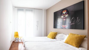 A hotel room with a large bed, two yellow pillows, a white chair, and a large painting on the wall. - Apartamentos Haro (Haro)