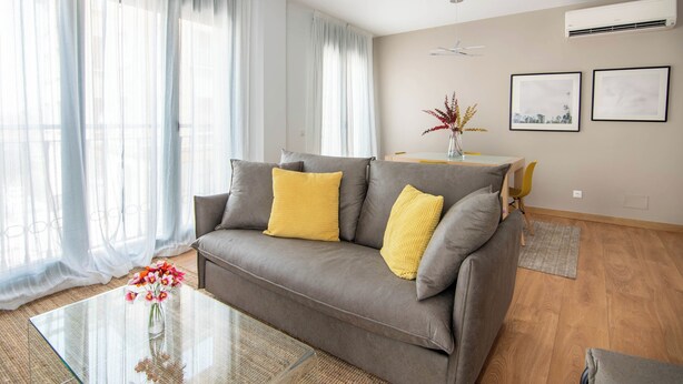 A modern living room with a grey sofa, yellow cushions, a glass coffee table, and a vase with flowers. - Apartamentos Haro (Haro)