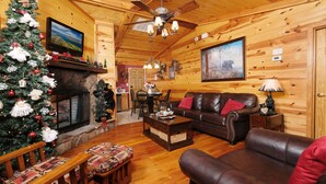 Ein gemütliches Blockhaus-Interieur mit Kamin, Ledersofa, Holzesstisch und einem Weihnachtsbaum.