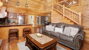 A wooden cabin interior with a living room, kitchen, and a staircase.