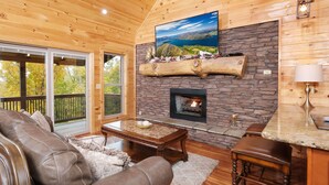A cozy living room with a stone fireplace, leather sofa, and a large window overlooking a scenic landscape.