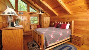 Camera accogliente di una baita con un letto di legno, un comodino, una lampada e una finestra vista verde.