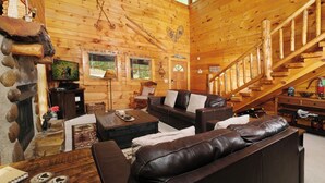 Accogliente interno di una baita in legno con camino, scala in legno, divani in pelle e televisore.