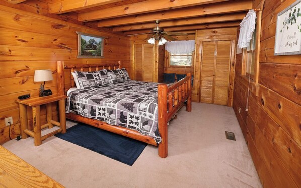 Un dormitorio de cabaña de madera con una cama, una mesita de noche, una lámpara y un ventilador de techo.