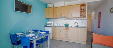 A compact kitchen with a dining area, featuring a microwave, sink, and wooden cabinets.